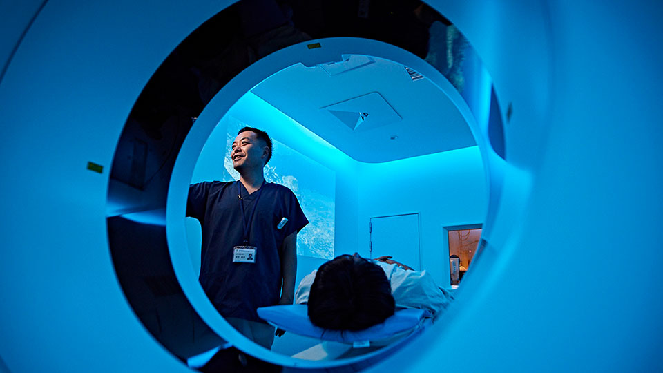 Foto van arts die een scan instelt bij het portaal van de CT-scanner, met de pati&euml;nt op de pati&euml;nttafel van het CT-systeem