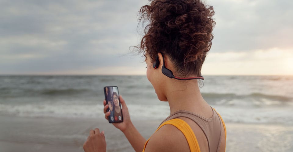 Atleet neemt een oproep aan op het strand terwijl hij bone conduction koptelefoon gebruikt
