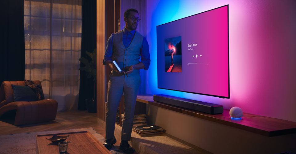 Persoon in een moderne woonkamer bij een Philips Ambilight-tv met muziekinterface en Fidelio-soundbar