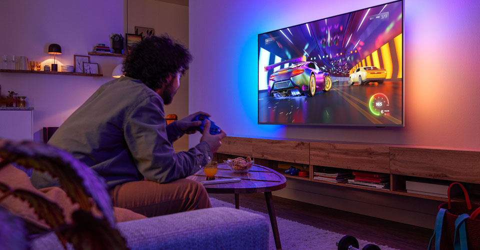 Een persoon zit op een bank en speelt een racespel op een Philips Ambilight-tv