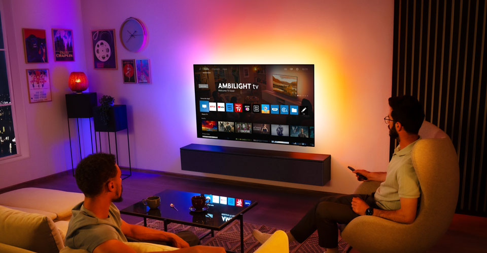 Twee mannen kijken naar een aan de muur gemonteerde Ambilight-tv in een woonkamer