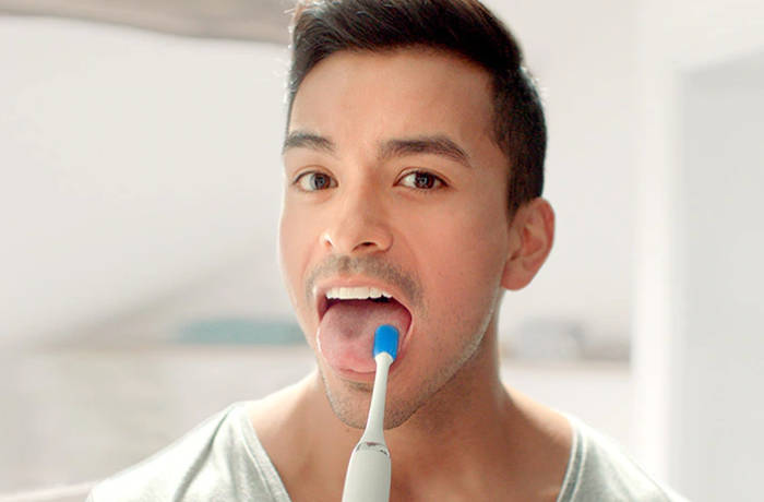 Een man maakt zijn tong schoon met een speciale Philips-tongborstel.